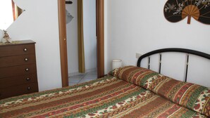 A bedroom with a bed, a dresser, a mirror, and a wall fan.