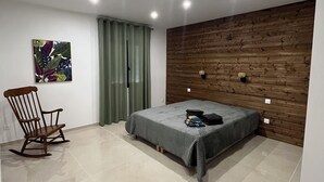 Ein modernes Schlafzimmer mit Bett, Schaukelstuhl, einer Wand mit Holzvertäfelung und Einbauleuchten.