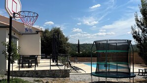 Ein Wohnbereich im Freien mit Basketballkorb, Trampolin, Pool und einer Terrasse mit Stühlen und Tischen.
