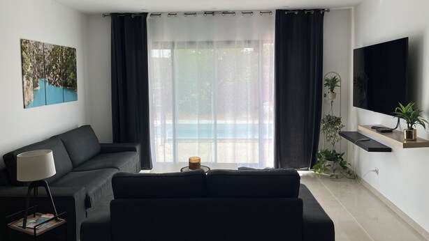Ein modernes Wohnzimmer mit einer Couch, einem Flachbildfernseher und Blick auf einen Pool.