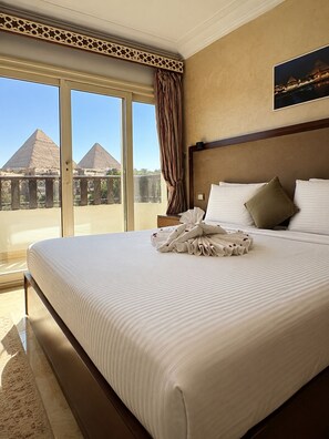 Une chambre d’hôtel avec un grand lit, une vue sur les pyramides et un balcon avec un rideau.