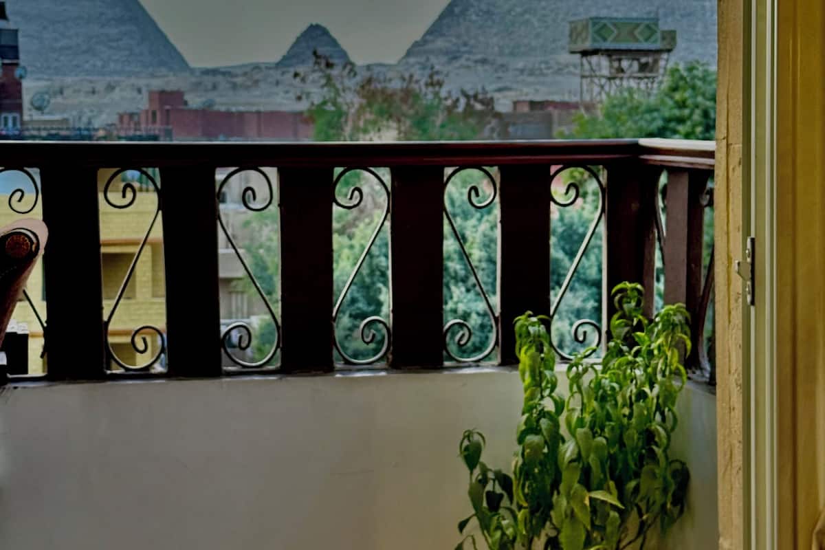 A balcony with a view of the pyramids, a potted plant, and a metal railing.