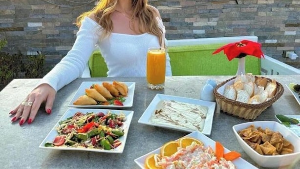 A person seated at a table with a variety of food items and a drink, with pyramids in the background. - Flower Pyramids Inn (Giza)