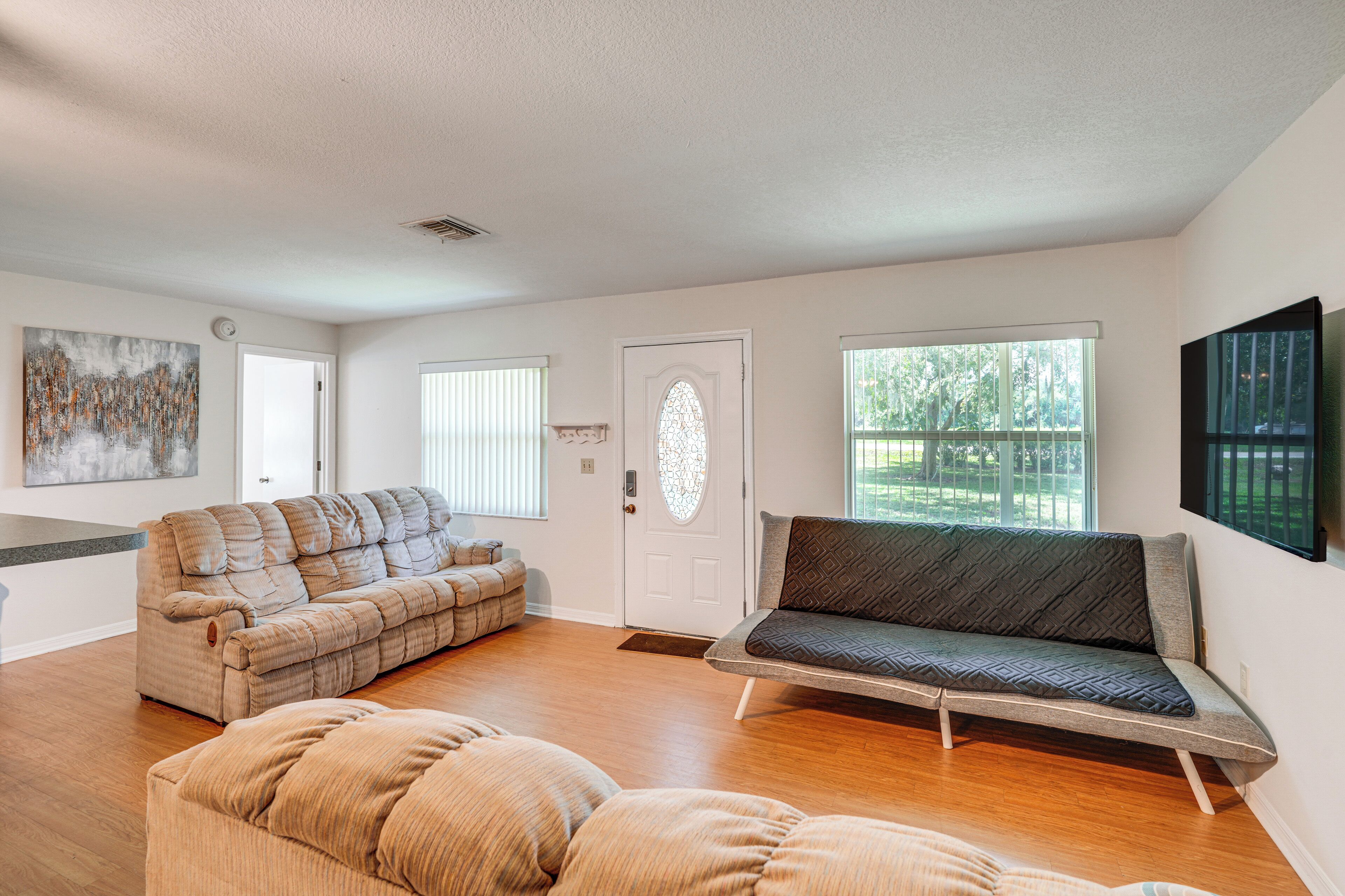A spacious living room with a large sectional sofa, a smaller sofa, and a bean bag chair. There is a large window providing natural light and a view of the outdoors.