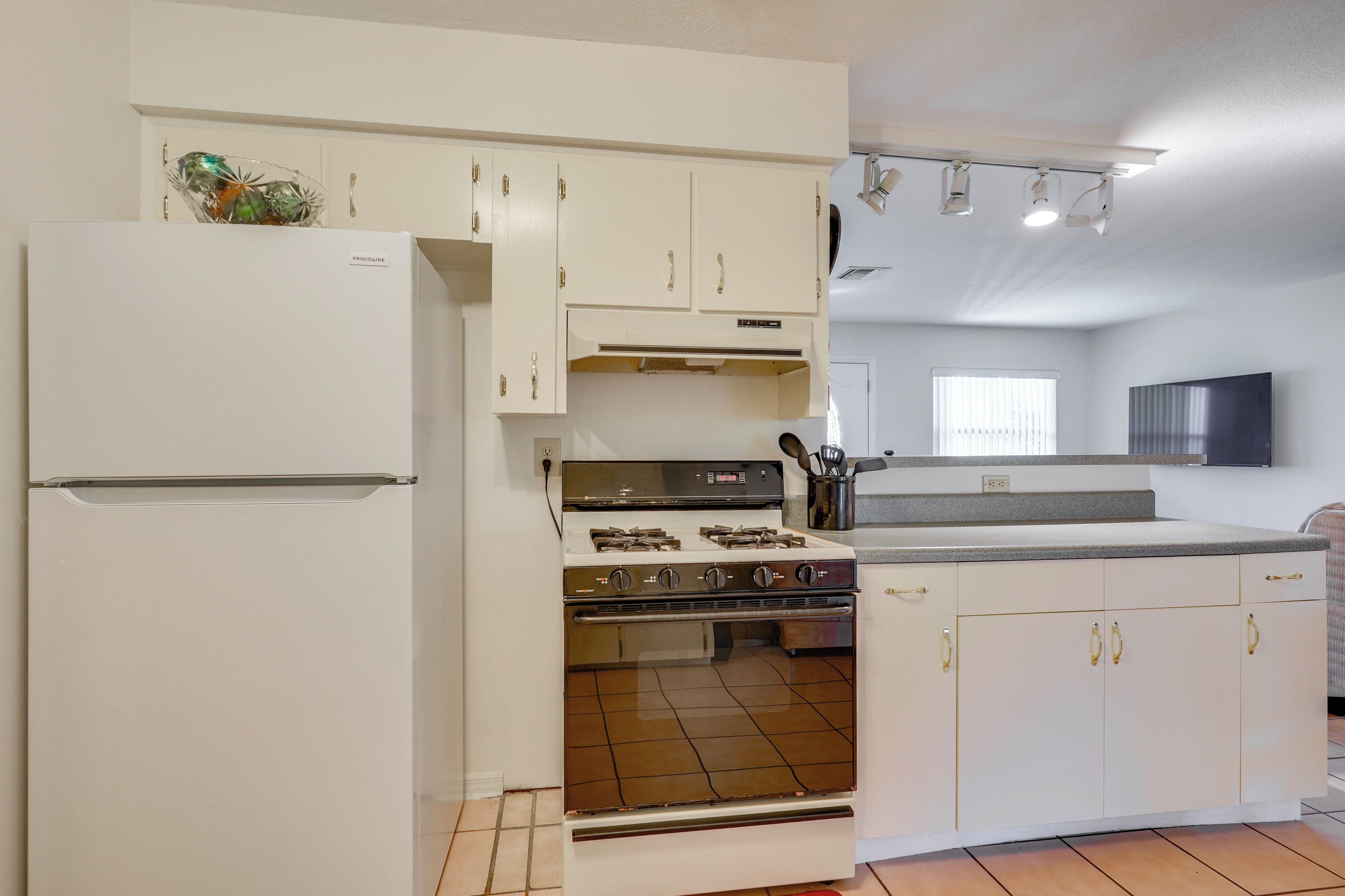 Cocina compacta con muebles blancos, estufa integrada y refrigerador.
