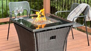 Taula de vidre amb foc central, envoltada de cadires de vimet al voltant d'un terraç de fusta.