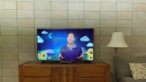 Televisor sobre un moble de fusta amb un disseny temàtic de cel nocturn, una làmpada i un sofà amb coixí floral.