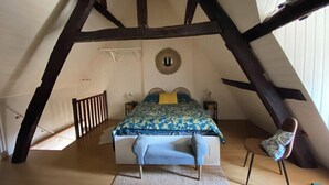 A bedroom with a sloped ceiling, a bed with a blue floral bedspread, a round mirror on the wall, and a small table with a lamp.