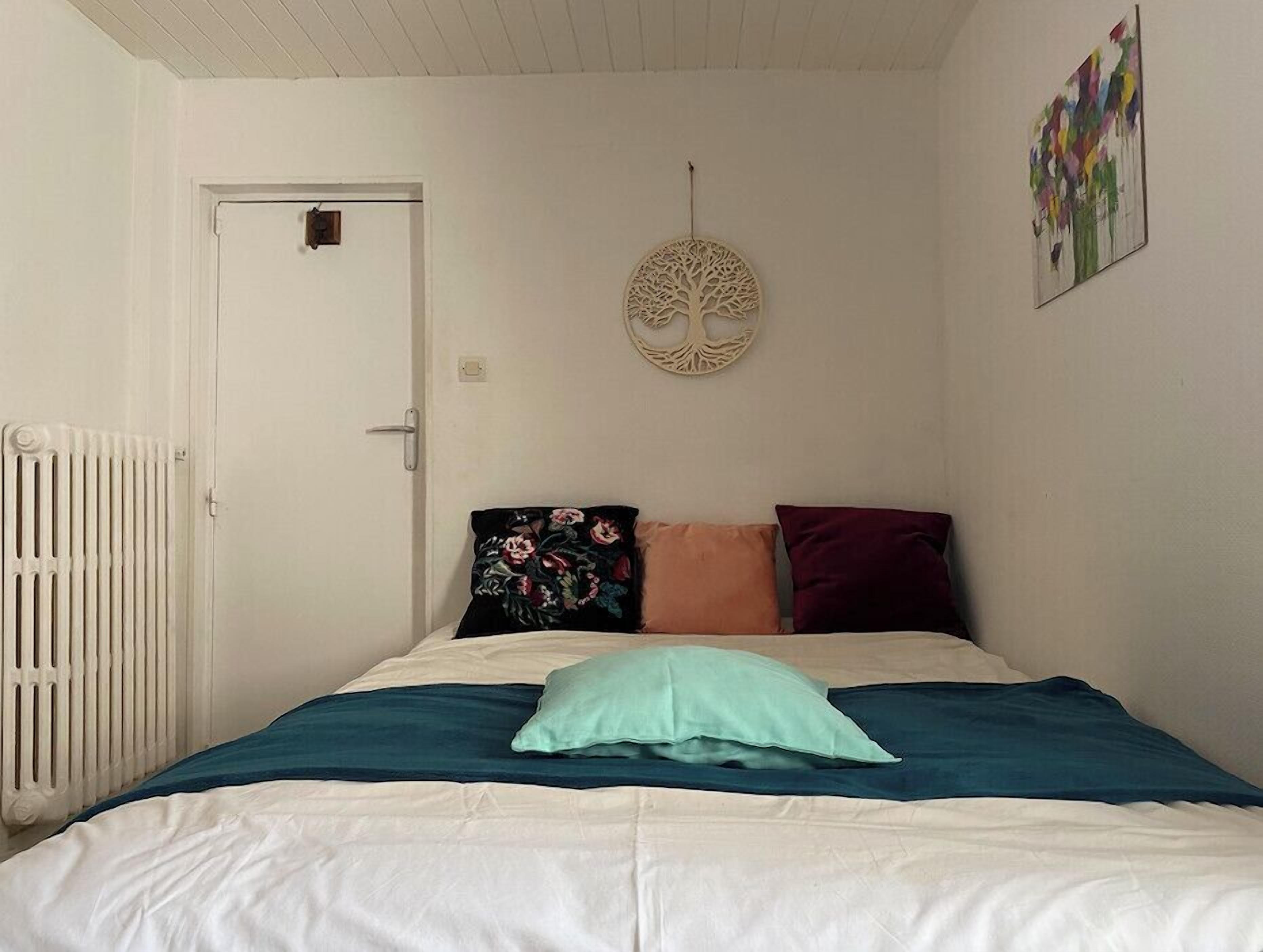 A bedroom with a bed, a radiator, a door, and a wall decoration.