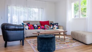A modern living room with a leather armchair, a sofa with colorful floral cushions, a wooden coffee table, and a small ottoman. - Pretty house with pool in Cagnes-sur-Mer (Cagnes-sur-Mer)