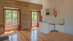 A modern kitchen with a built-in microwave, a sink, and a compact refrigerator. There are two double doors leading to a balcony with a view of greenery. - Feel Discovery Casa da Granja I (Resende)