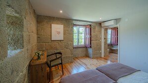 Une chambre avec des murs en pierre, un bureau en bois, une chaise, un lit avec une couverture et une fenêtre donnant sur l’extérieur.