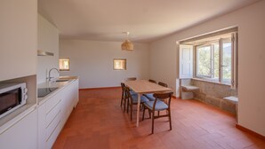 Eine Küche mit Mikrowelle, Spüle und Esstisch aus Holz mit Stühlen. Ein Fenster bietet Blick auf Bäume.