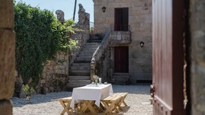 Ein Gebäude aus Stein mit einer Treppe zu einem Balkon, einem Tisch mit Stühlen und einem kleinen Garten.