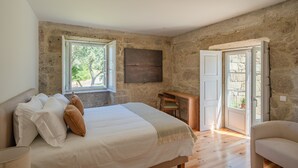 Une chambre avec un mur en pierre, un lit avec une literie blanche, un bureau en bois et une chaise.