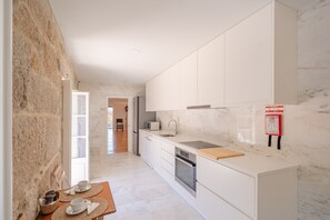 A modern kitchen with white cabinets, a marble countertop, and a wooden table with cups and saucers.