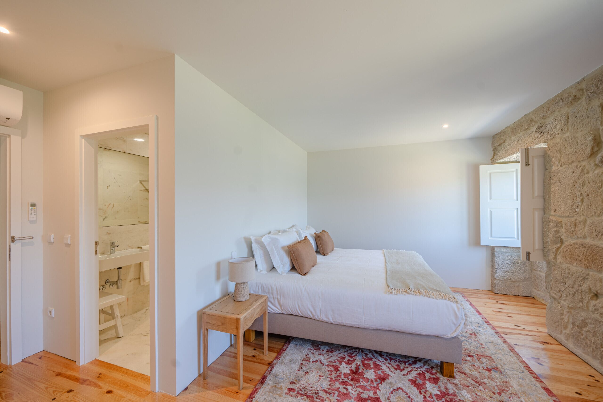 A bedroom with a bed, bedside table, and a bathroom visible through an open door.