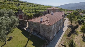 Un bâtiment en pierre, surmonté d’un toit de tuiles rouges, entouré d’un vignoble et d’un petit jardin.