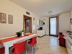 A compact room with a dining table, chairs, a small kitchenette, and a door leading to another room. - Residence Tulipano three-room apartment Tipo C* for 6 persons (Bibione)