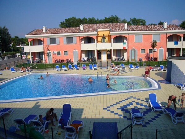 A swimming pool area with multiple lounge chairs and a building with balconies in the background.