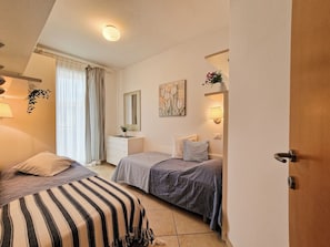 A bedroom with two beds, a dresser, a mirror, a painting, and a plant.