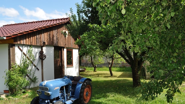 Un tractor blau estacionat davant d'un edifici rústic amb teulada vermella.