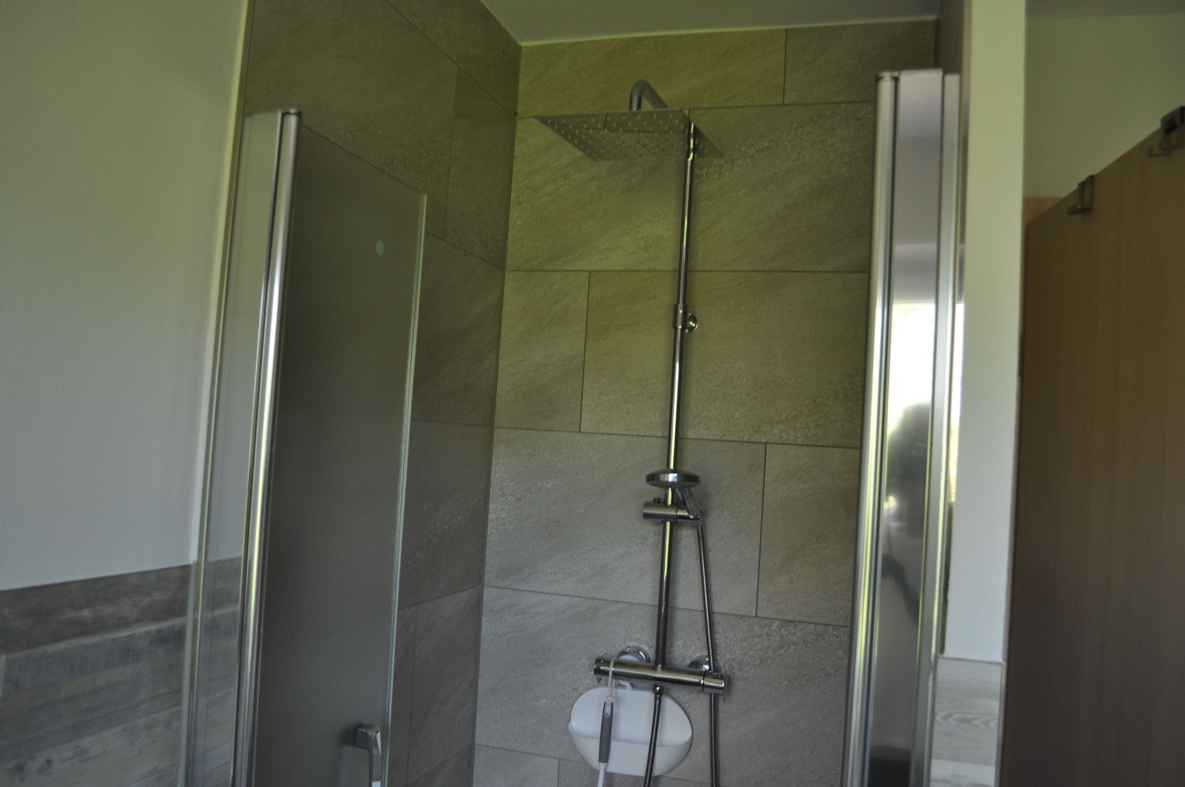 A shower area with a glass door, a showerhead, and a handheld shower attachment.