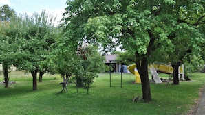 Un parc amb gespa verda, arbres i una estructura de joc groga.