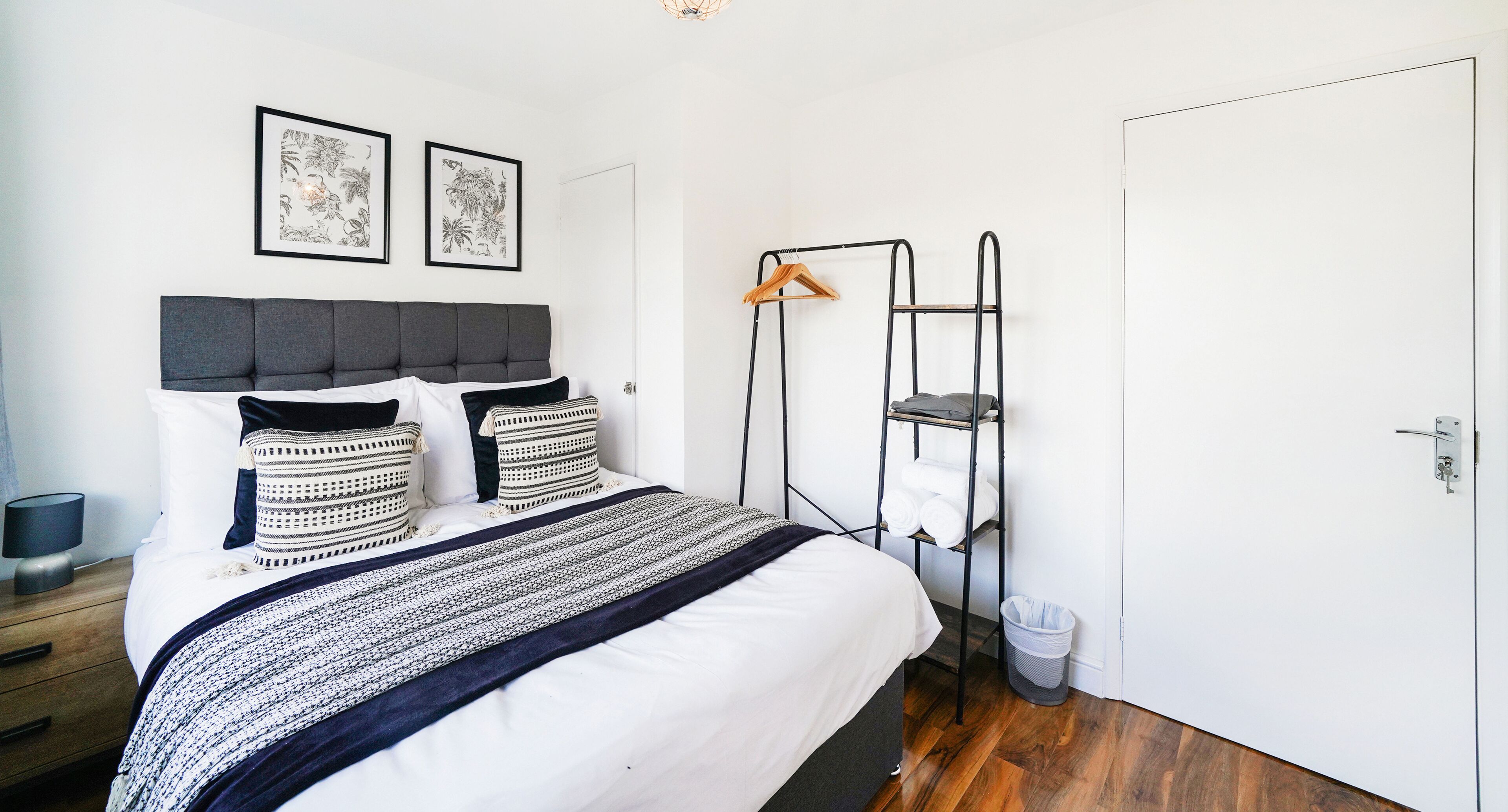 A neatly arranged bedroom with a bed, a bedside table, a wall-mounted shelf, and a door.