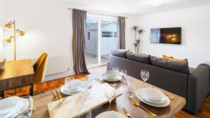 A modern living room with a dining area, a sofa, a TV, and a view of the outside. - Brabon Road House By REDWOOD STAYS (Farnborough)