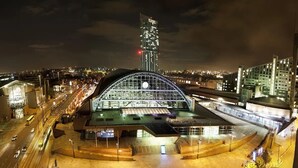 A modern building with a large glass facade and a curved roof, surrounded by a well-lit urban area with roads and other buildings. - Brabon Road House By REDWOOD STAYS (Farnborough)
