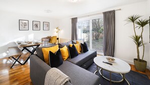 A modern living room with a grey sofa, yellow and black cushions, a round coffee table, and a dining area with a wooden table and chairs. - Brabon Road House By REDWOOD STAYS (Farnborough)