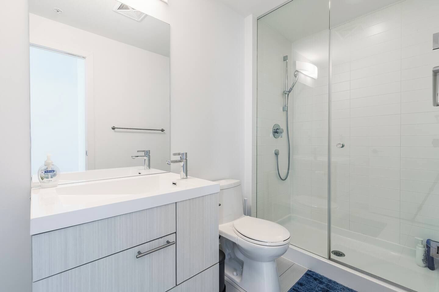 A modern bathroom with a white sink, mirror, and toilet, and a glass-enclosed shower area.