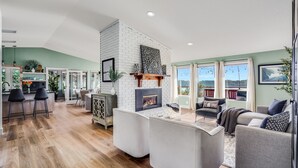 Een moderne woonkamer met een open haard, een keuken met barstoelen en uitzicht op het omliggende landschap.