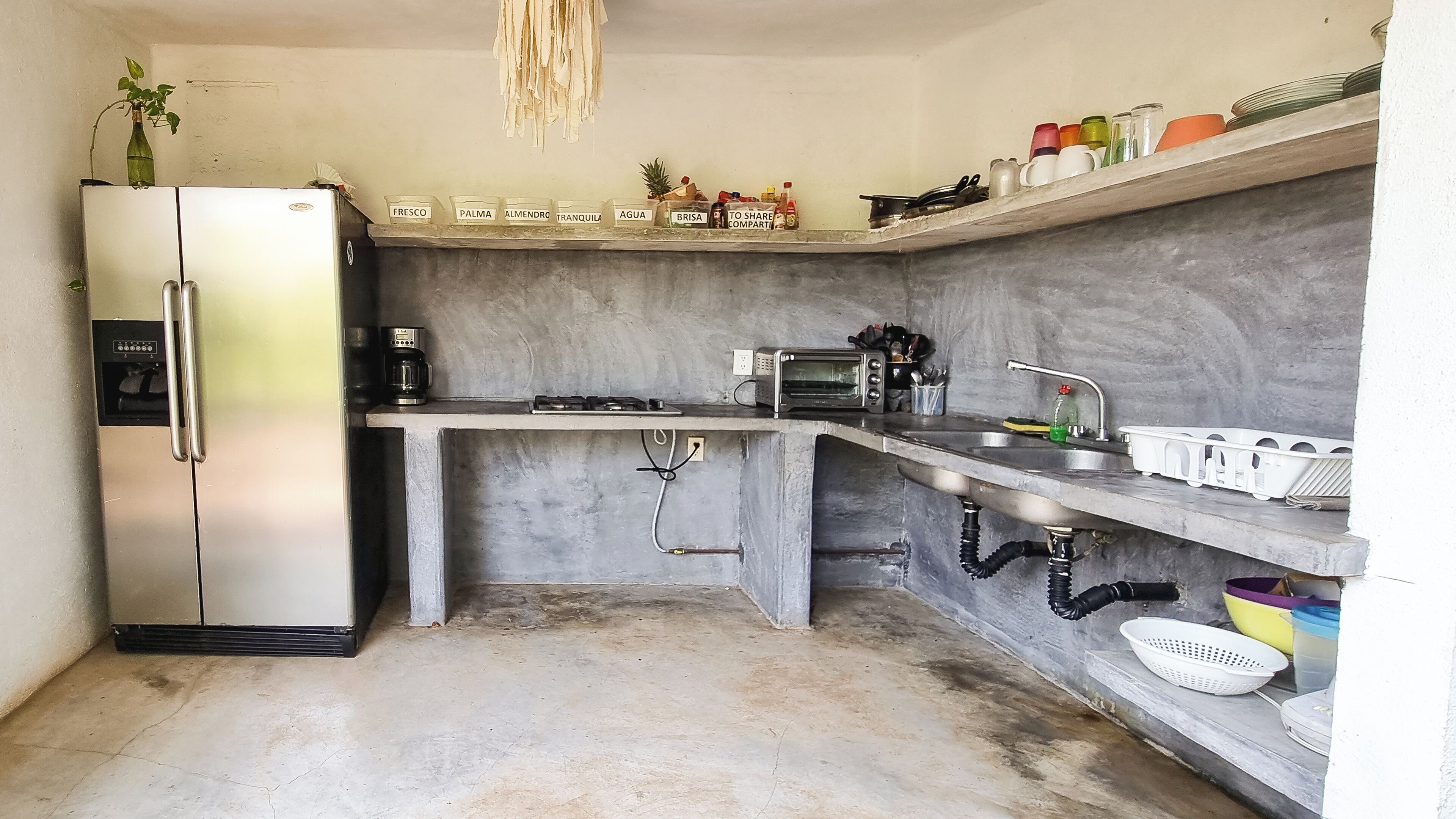 Cocina compacta con refrigerador, cafetera, tostadora, pileta y varios contenedores de almacenamiento.