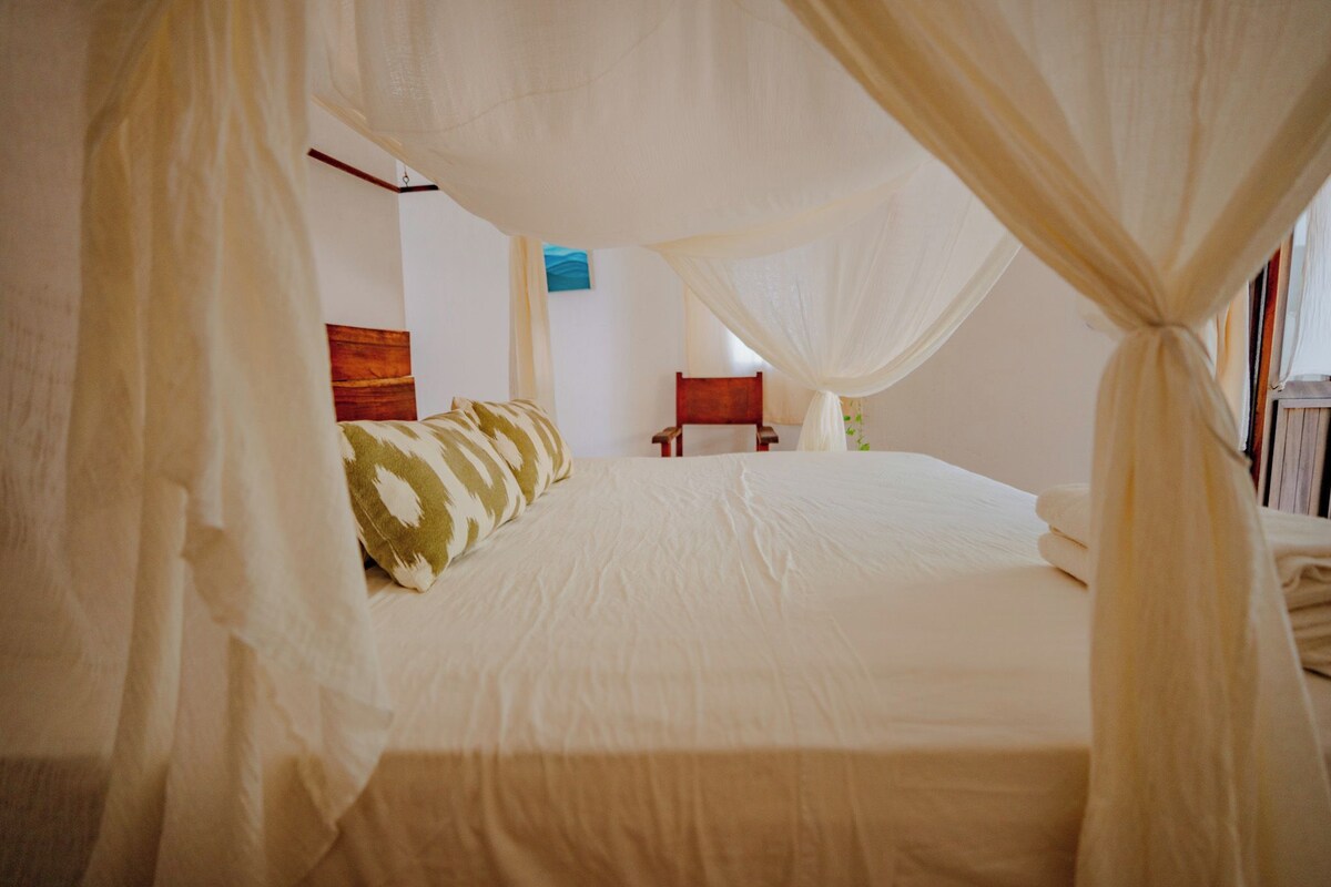 A bedroom with a canopy bed, a wooden headboard, a nightstand, and a wall-mounted painting.