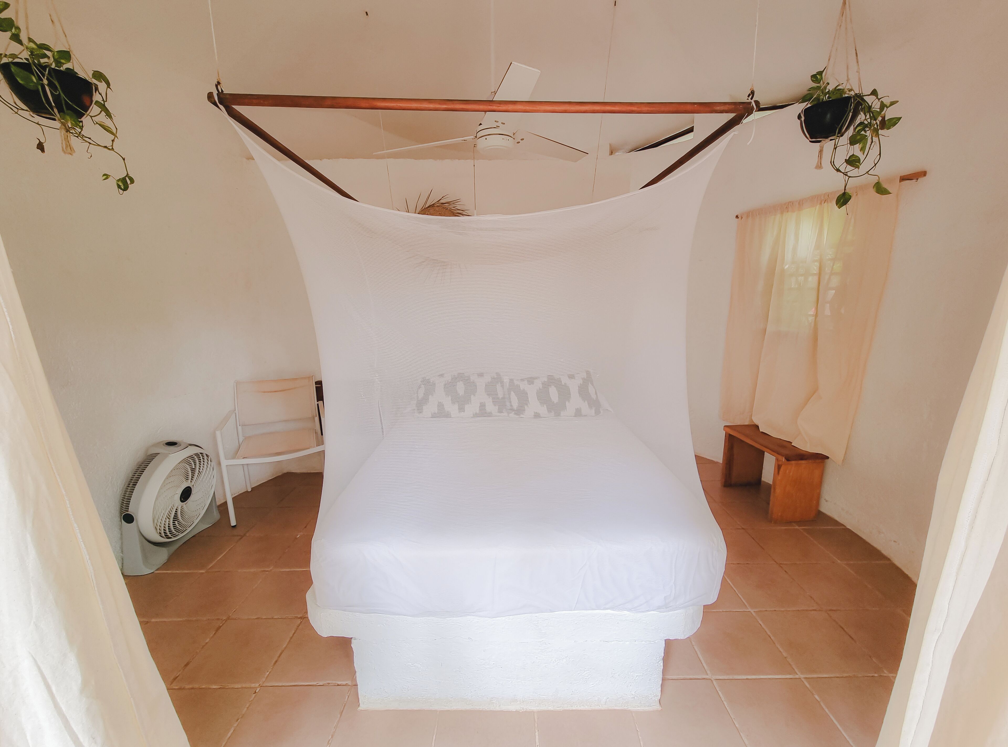 Uma cama de solteiro com dossel, um ventilador de teto e uma pequena mesa de cabeceira.