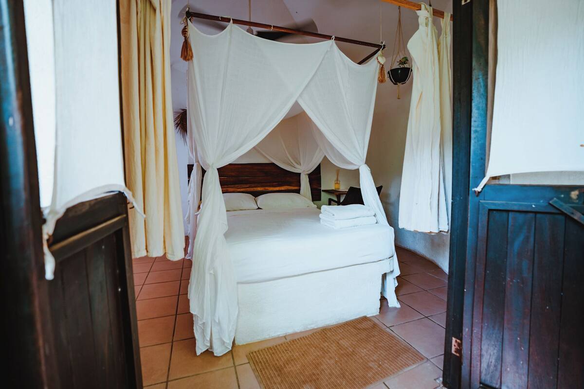 Ein Bett mit Baldachin, ein Nachttisch und ein kleiner Blumentopf.