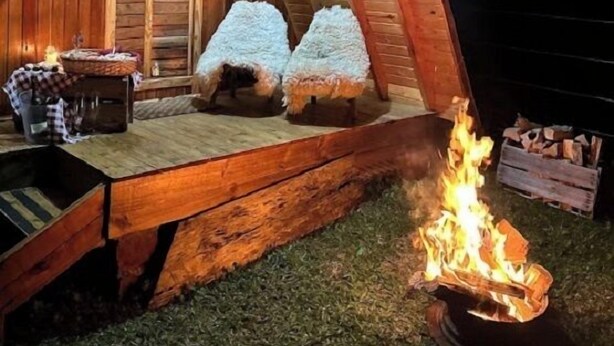 A wooden A-frame structure with a fire pit and two insulated sleeping areas. - Aldeia Colibri (Jaquirana)