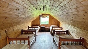 A long, narrow room with wooden walls and a sloped ceiling, containing four wooden beds aligned along the center. - Aldeia Colibri (Jaquirana)
