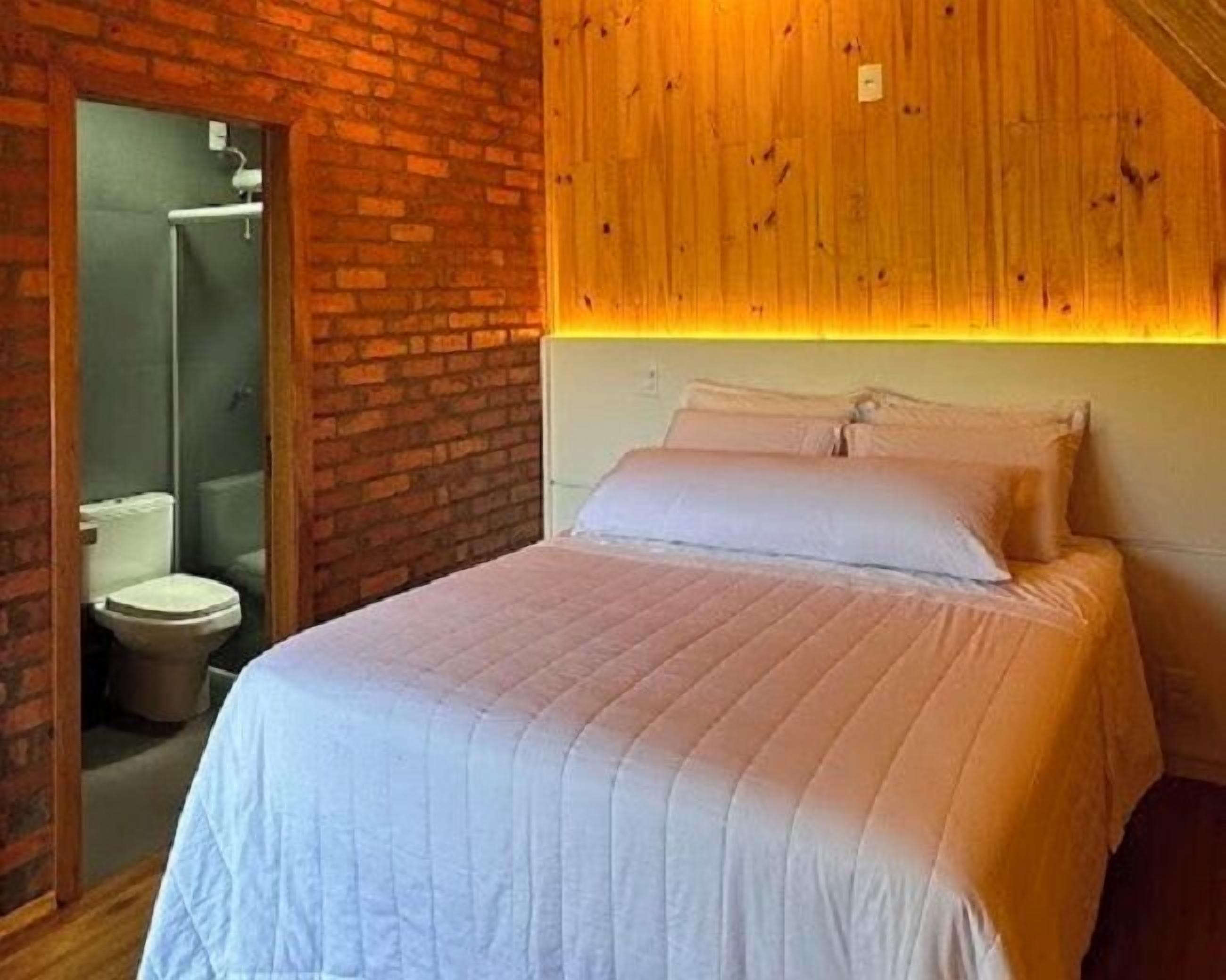 A bedroom with a brick wall, wooden ceiling, and a bed with white bedding.