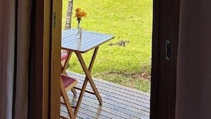 A wooden deck with a table and a vase of flowers, overlooking a green field. - Aldeia Colibri (Jaquirana)