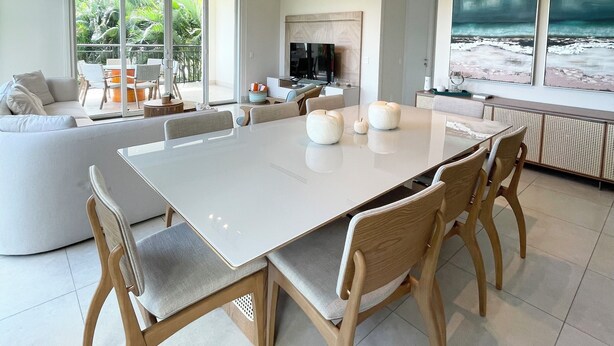 Un espace repas moderne avec une grande table, des chaises en bois et une vue sur l’extérieur grâce à de larges fenêtres.