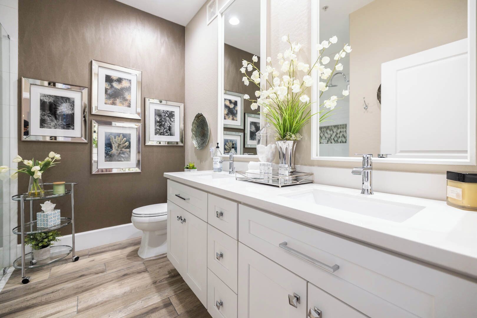 Une salle de bain moderne avec un meuble-lavabo blanc, un grand miroir et des œuvres d’art encadrées accrochées au mur.