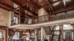 Ein großzügiger Wohnbereich mit hoher Decke, einer Treppe zu einer oberen Ebene und verschiedenen Sitzmöglichkeiten, darunter ein Sofa und Sessel.