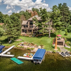 A large, multi-story stone house with a well-maintained lawn, a dock with boats, and a small boat house. - Church Pine Lodge in Osceola (Osceola)