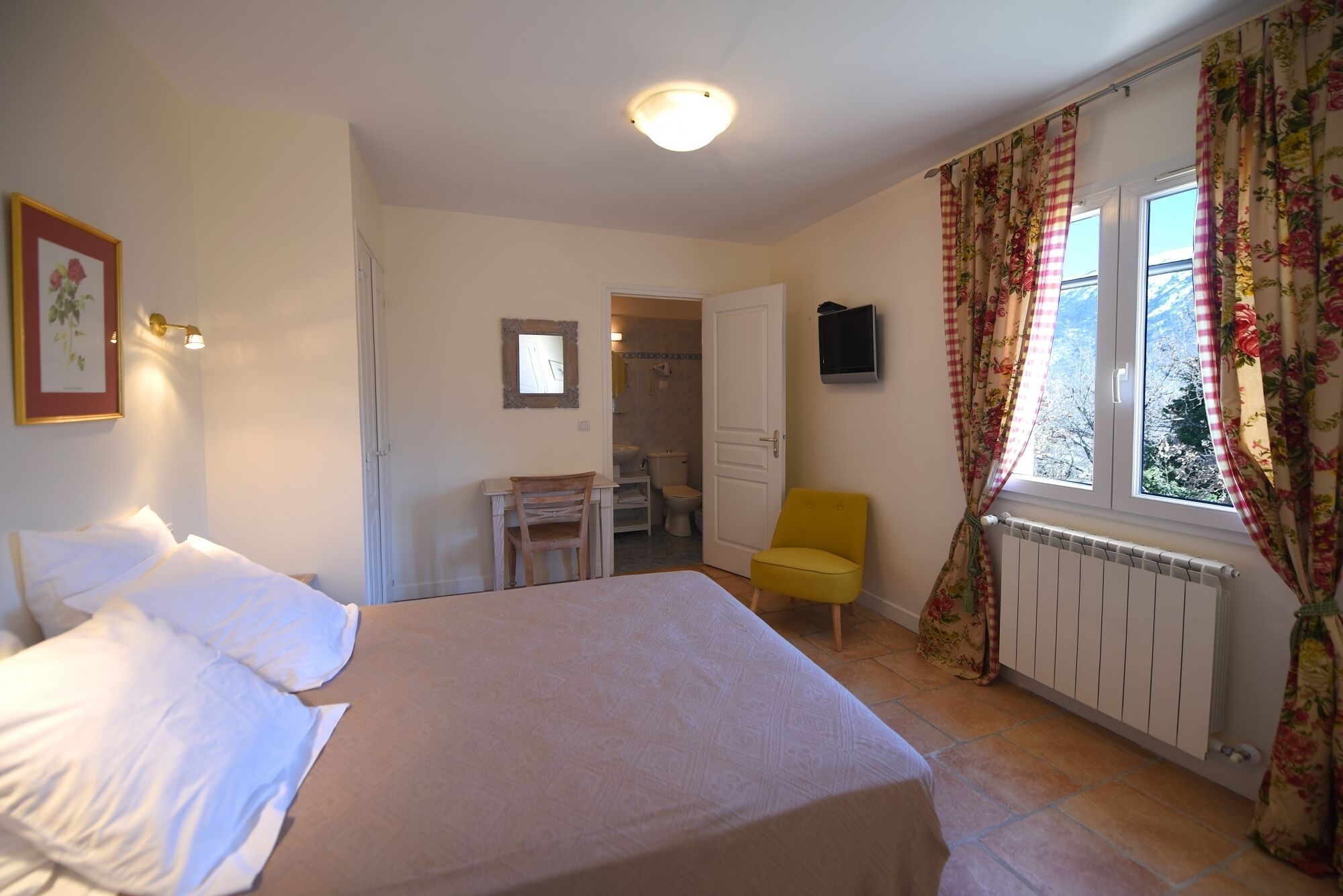 Un dormitorio con cama, una silla, un escritorio y un baño visible a través de una puerta abierta.