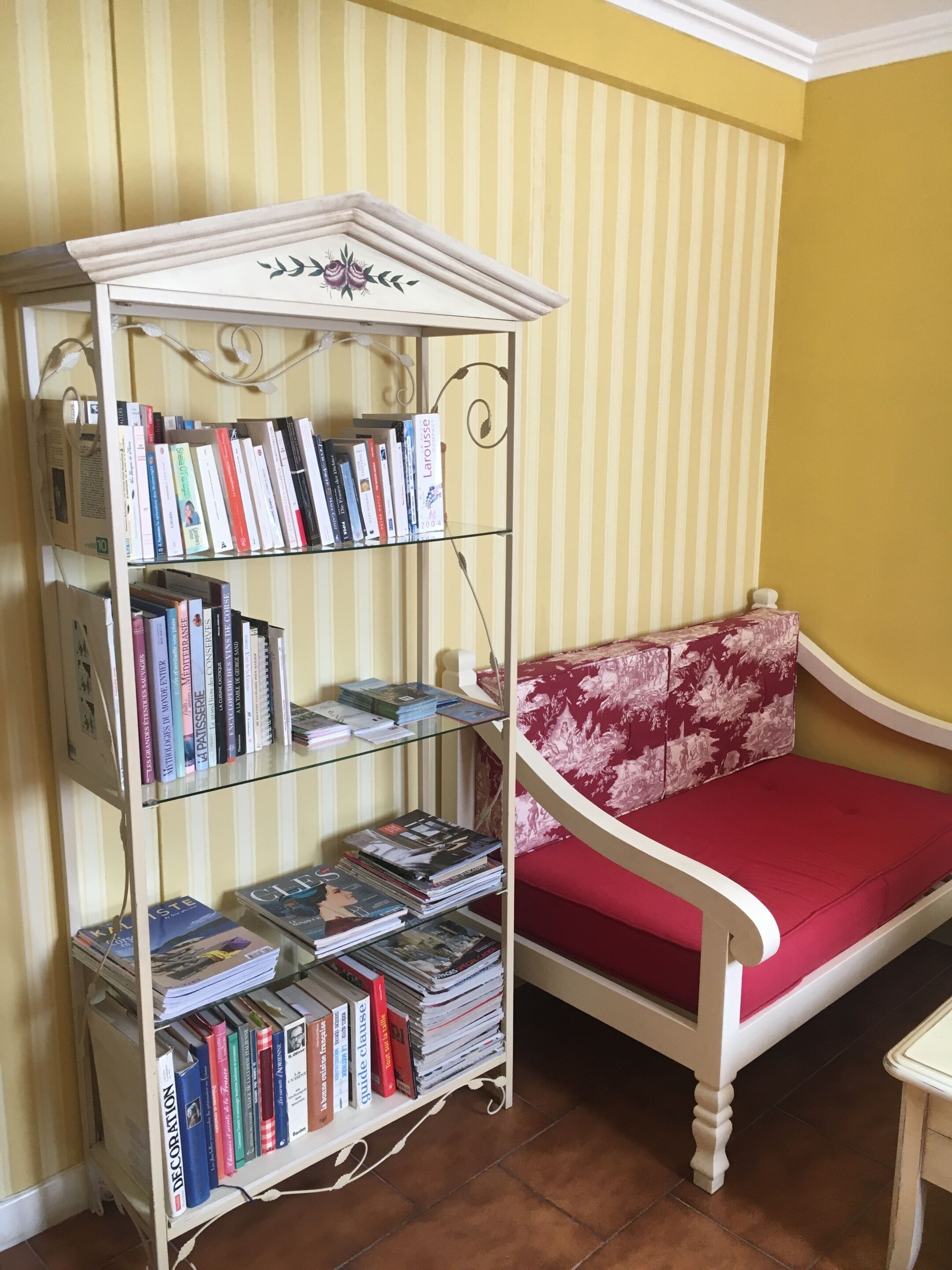 A corner with a white bookshelf filled with books, a red floral sofa, and a yellow striped wall.