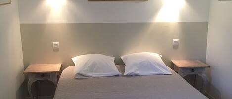 A bedroom with a bed, two bedside tables, a nightstand, a wooden chair, and a painting on the wall.