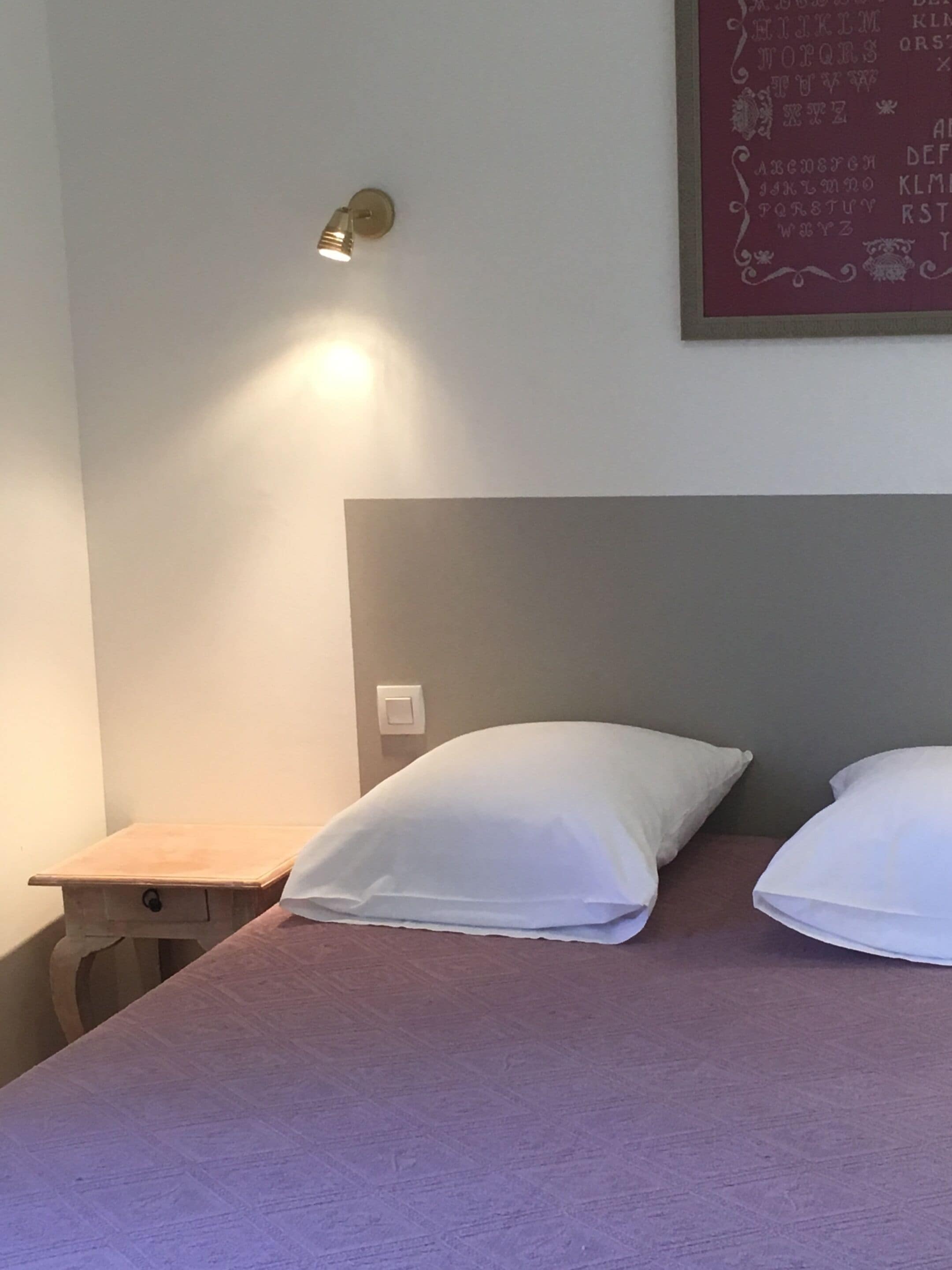 A bedroom with a bed, two pillows, a nightstand, and a wall-mounted light fixture.